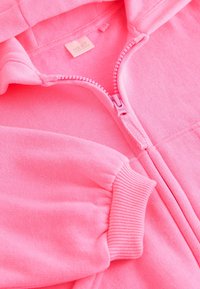 Minkštas rožinis džemperis su megztu rankogaliu, dalinai atsegamu užtrauktuku ir matoma prekės ženklo etikete ant apykaklės viduje.