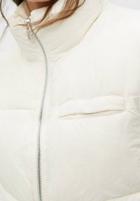 Weiße gepolsterte Jacke mit hohem Kragen, Frontreißverschluss und kleiner Brusttasche. Glatte Textur und leichtes Design.