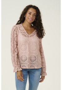 Blusa in pizzo rosa con scollatura a V, dettagli floreali intricati, maniche lunghe a palloncino con polsini volant e vestibilità rilassata. Abbinate a jeans blu.