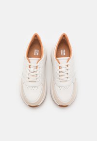 Hvite sneakers med en glatt lær øvre, oransje detaljer på innsiden, og en strukturert beige såle med perforerte detaljer.