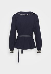 Mörkblå långärmad blus med volangkrage, peplummidja och broderade manschetter. Har ett knytband på baksidan för en tajt passform.