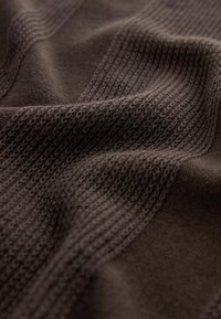 Tissu brun foncé texturé avec un motif côtelé et des sections en tricot ajouré, présentant des profondeurs variées et une texture douce et lisse.