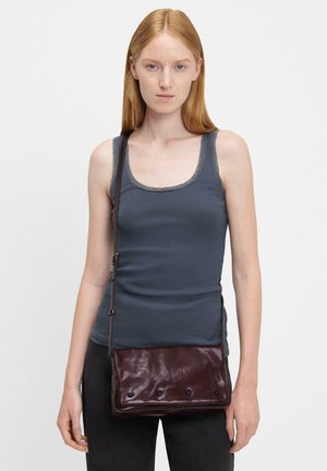 Eine dunkelburgunderfarbene Leder Crossbody-Tasche mit glatter Textur, ausgestattet mit einem Vorderklappenverschluss und fünf Knopfakzenten. An der Schulter eines Models getragen.