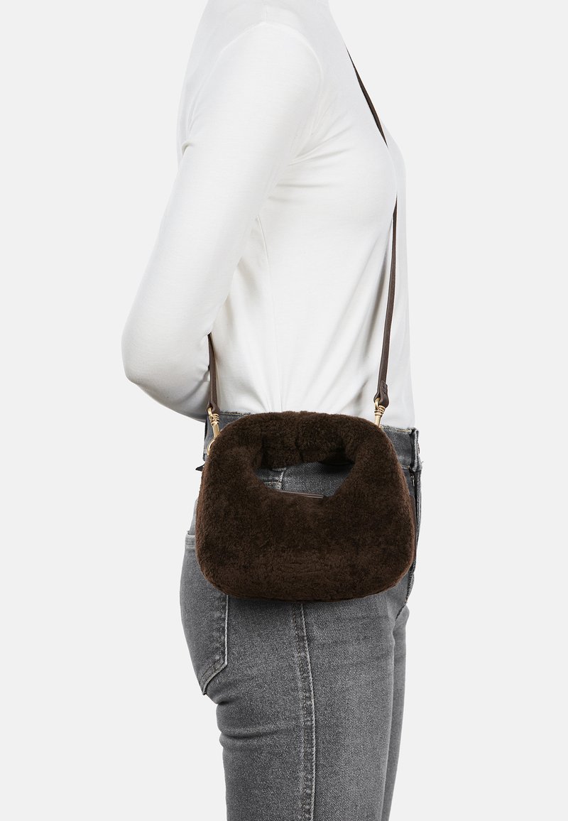 Brown plush crossbody bag with a rounded shape, featuring a soft texture and a brown strap. Gold hardware accents are visible.