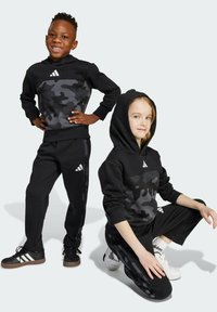 Czarny komplet z kamuflażem - bluza z kapturem i spodnie, z prążkowanymi mankietami, przednią kieszenią i białym logo Adidas. Zawiera dopasowane czarne obuwie.