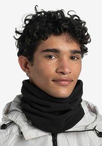 Gaiter de cuello de forro polar negro con una textura suave, que presenta múltiples pliegues y costuras, usado por una persona con una chaqueta blanca ligera.