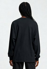 T-shirt noir à manches longues en coton doux, avec une coupe décontractée, un col rond et des poignets côtelés. Aucun motif ou graphique visible.