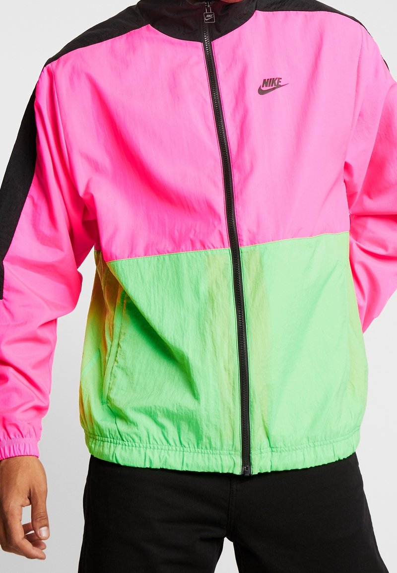 Nike vindjacka i rosa och grönt, med dragkedja framtill, ståkrage och elastiska ärmslut. Slät, lättviktig material.