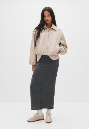 Beige zip-up bomber jacket, harmaa villa maksi hame ja vaaleanpunainen kerroksellinen paita. Vaaleat kengät nauhoilla ja teksturoidut harmaat sukat.