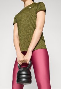 Persona con camiseta deportiva verde y leggings rosas sosteniendo una pesa rusa negra con ambas manos frente a ellos.