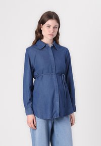 Camisa de denim azul escuro com fecho com botões à frente, mangas longas e um cinto laço na cintura. Textura suave e design de colarinho clássico.