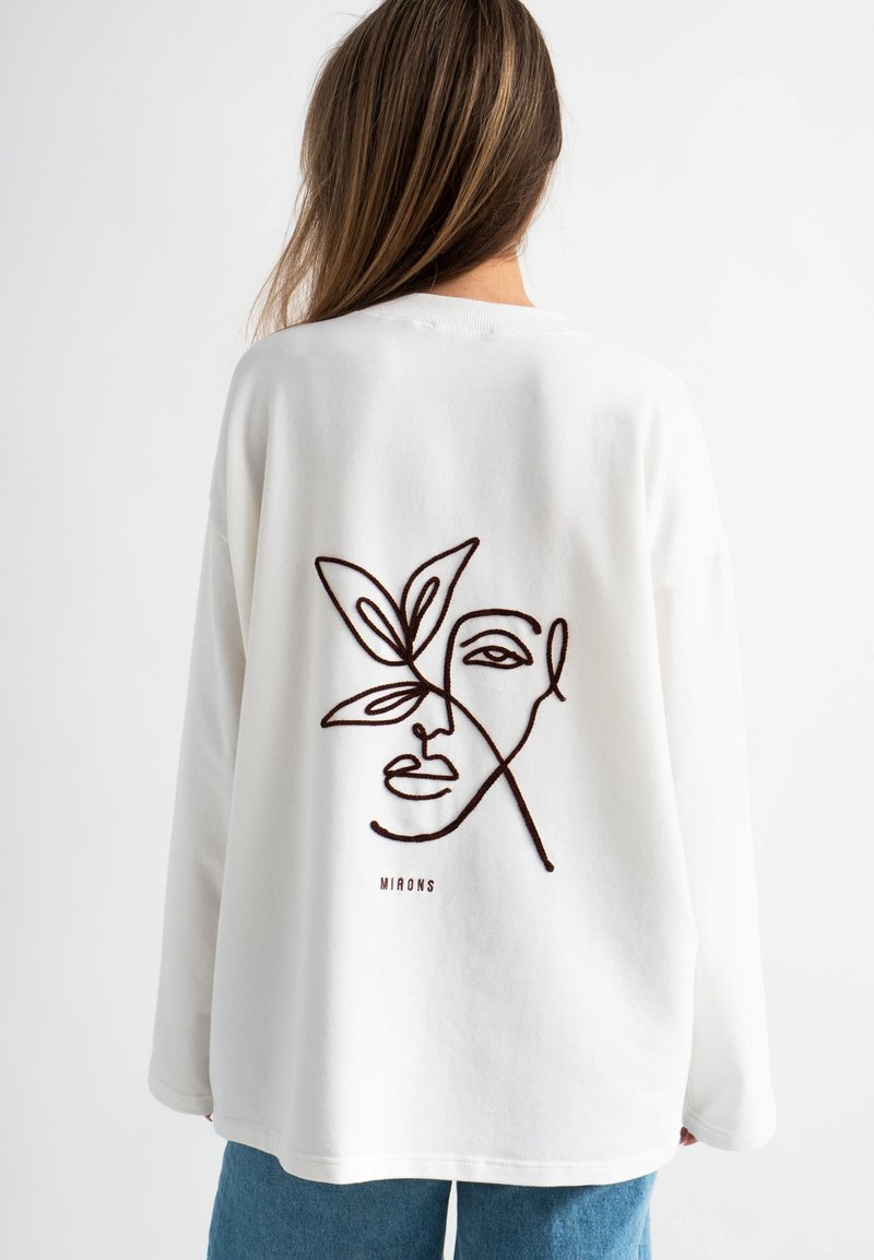 Witte sweatshirt met een bruin lijn-tekening gezicht en bladvorm ontwerp op de achterkant. Lange mouwen en een ontspannen pasvorm. Minimalistische esthetiek.