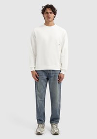 Witte sweatshirt met ronde halslijn, ribgebreide manchetten en zoom. Draagt met lichtblauwe jeans en zilveren sportschoenen. Minimalistisch ontwerp.