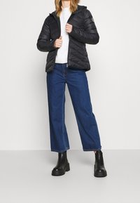 Svart pufferjacka med huva, med quiltad design och dragkedjestängning. Kombinerad med högmidjade blå denimbyxor och svarta klumpiga stövlar.