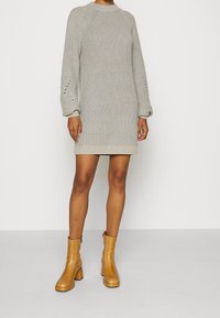 Abito lavorato a maglia grigio chiaro con una texture a coste, maniche raglan e motivi decorativi a fori, abbinato a stivali alti con tacco a blocco color beige.