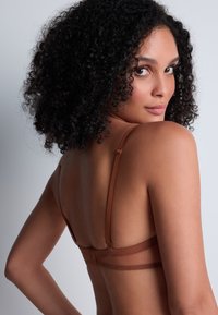 Bralette brun transparent avec des bretelles réglables, présentant une texture lisse et un design minimaliste, vue de dos.