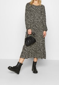 Femme portant une robe midi à imprimé léopard noir et blanc, des bottes de combat noires à lacets, tenant un petit sac à main noir.