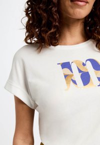 Witte t-shirt met korte mouwen, voorzien van een grote grafische print in blauw, goud en crème. Ronde halslijn en omgeslagen mouwen.