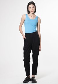Canottiera azzurro chiaro con pizzo abbinata a pantaloni cargo neri con tasche laterali e vestibilità aderente, completata da scarpe nere.