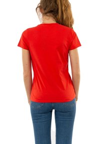 Camiseta roja de algodón con un diseño ajustado y mangas cortas, vista desde atrás. Combinada con jeans de mezclilla azules.