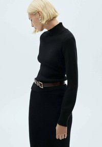 Maglione nero a coste con un colletto alto, design aderente e maniche lunghe. Abbinato a una cintura marrone con fibbia in metallo.