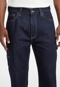 Pantalones cargo de denim oscuro con corte recto, featuring costuras en contraste, múltiples bolsillos y un cierre clásico de botón en la parte delantera.