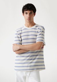 Camisa de manga corta a rayas en blanco con rayas horizontales azules, que presenta un patrón de punto texturizado y un cuello redondo.