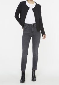 Black button-up cardigan over a white t-shirt, paired with gray high-waisted jeans and black ankle boots. Smooth textures, fitted design.