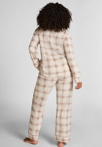 Pluche geruite pyjama's in beige en bruine tinten. Langsleeve top met een rechte snit en bijpassende broek met een relaxte pasvorm en omgeslagen boorden.