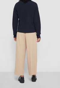 Stickad marinblå tröja med ett strukturerat mönster, i kombination med vida beige byxor och svarta platåskor, sedd bakifrån.