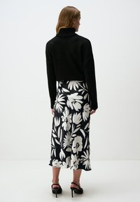 Zwarte coltrui, cropped fit. Vloeiende, knielange rok met grote witte bloemenpatronen op een zwarte achtergrond. Zwarte hoge hakken sandaaltjes.