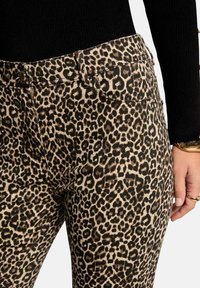 Jeans de estampado de leopardo con una base beige y manchas negras, forma estructurada, cinturilla de altura media y bolsillos frontales para un detalle adicional.