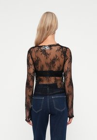 Svart blonde langermet topp med blomstermønster, gjennomsiktig tekstur, rund hals, og en cropped design, sammen med mørke denimjeans.
