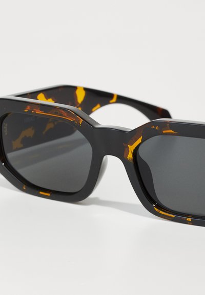 Black sunglasses with tortoiseshell pattern accents, chunky rectangular frame, dark lenses, smooth surface, and prominent hinges.