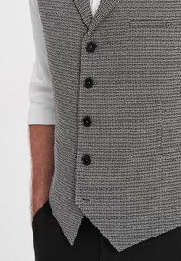 Chaleco gris con un patrón y un acabado texturizado, que presenta cinco botones negros, un fondo puntiagudo y un detalle de bolsillo en la parte frontal.