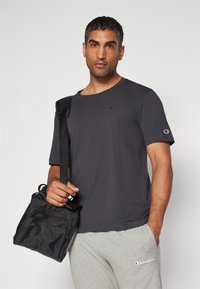 Mørkegrå kortærmet t-shirt med rund halslinning og et lille logo på brystet, parret med lysegrå sweatpants og en sort skuldertaske.
