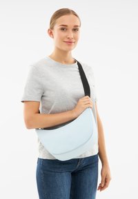 Borsa a tracolla azzurro chiaro realizzata in materiale morbido, con una forma curva e una tracolla nera. Nessun motivo o dettaglio in metallo visibile.