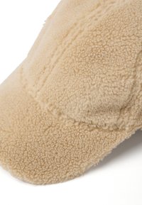 Cappello di pile beige con una consistenza morbida, dotato di una visiera strutturata e motivi cuciti sulla superficie.