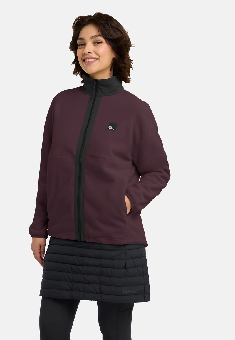 Bordeaux fleece jack met hoge kraag, voorrits en zwarte accenten; gedragen met een gestructureerde zwarte puffer rok en leggings.