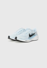 Baskets de sport bleu clair avec une tige en mesh, logo swoosh noir, semelle blanche rembourrée et semelle extérieure en caoutchouc noir texturé.