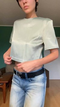 Hellgrünes, cropped Top aus glattem, halbtransparentem Stoff mit kurzen Ärmeln. Getragen mit blauen Jeans und einem schwarzen Gürtel, was einen lässigen Look unterstreicht.