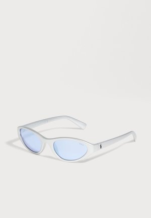 Lunettes de soleil blanches œil-de-chat, avec des verres bleu pâle et des branches fines, sur un fond clair.