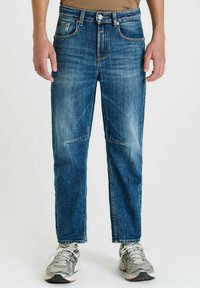 Donkerblauwe denim jeans met een rechte pijp, voorzakken en subtiele vervaging. Gecombineerd met grijze sportschoenen.