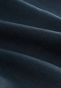 Dark blue fabric with a smooth, slightly textured surface, showing soft, flowing folds and subtle variations in color depth.