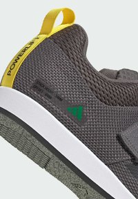 Siva atletska obuća s mrežastim gornjim dijelom, žutim petnim nastavkom i bijelim potplatom. Ima oznaku koja detaljno prikazuje visinu slojeva i mjere offseta.