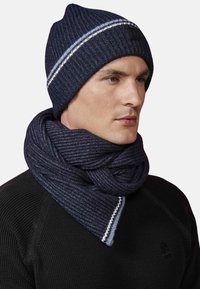 Beanie a coste blu marina con striscia bianca, abbinato a una sciarpa coordinata con un motivo testurizzato, entrambi realizzati in materiale lavorato a maglia.
