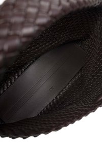Interno di una borsa intrecciata marrone con una base in pelle nera liscia. Presenta cuciture discrete e un piccolo logo in rilievo sulla pelle.