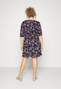 Vestido floral com fundo preto, apresentando mangas curtas e uma bainha com volantes. As cores incluem roxo, rosa e verde. Exibido de costas.
