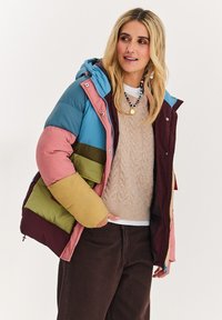 Barevná prošívaná bunda s panely v modré, růžové, zelené a bordo barvě, s kapucí a zapínáním na zip. Viditelná texturovaná vnitřní podšívka.