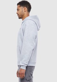Gray cotton hoodie with a front pocket, ribbed cuffs, and a drawstring hood. Model shown in profile against a plain background.